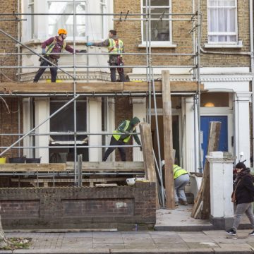 Four workers collaborate to build a scaffold during the refurbishment of a residential premises