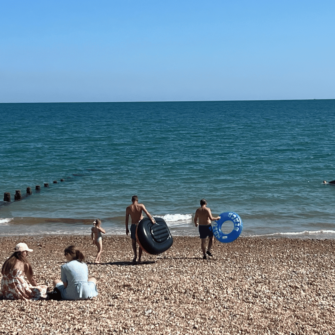People on a pebbled beach; two carry inflatable rings towards the sea, others sit or walk nearby under a clear sky.
Website Design Bognor Regis And Web Design West Sussex